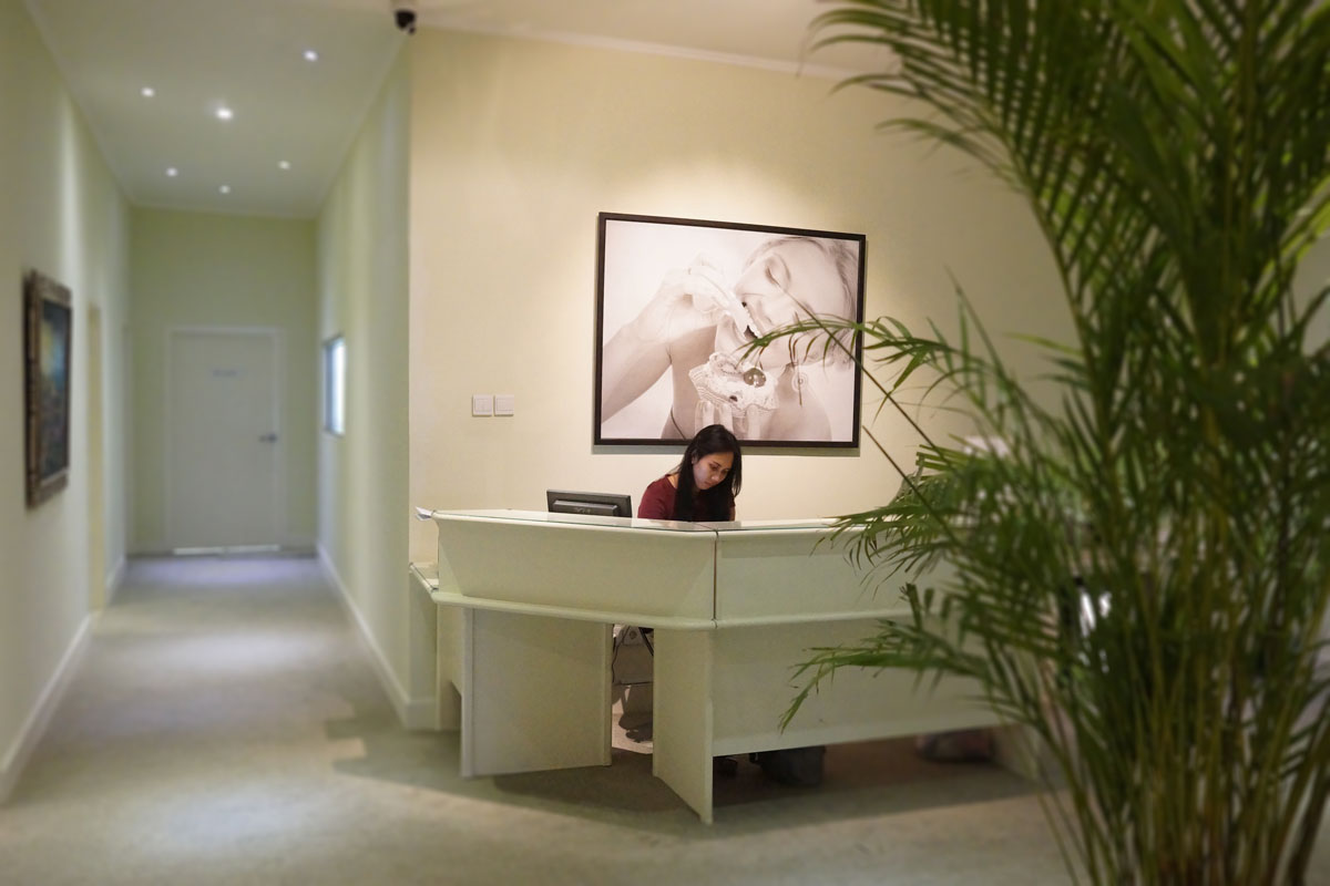 ARC Dental Bali receptionist at front desk in warmly lit clinic lobby with tropical decor