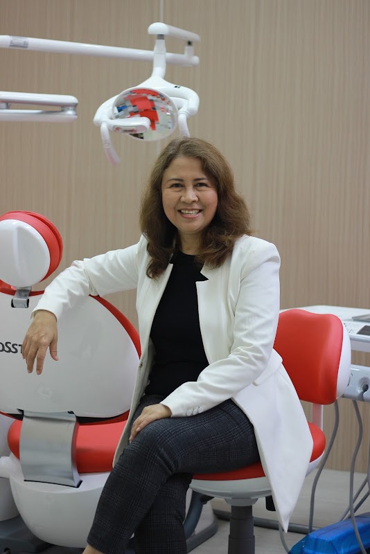 Smiling Kuta Dental female dentist in white coat seated beside a modern red dental chair