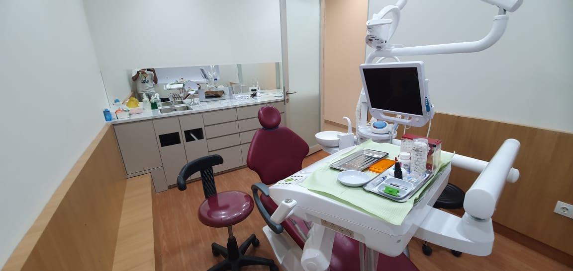 Dental treatment room at Rata Clinic with burgundy chair, digital monitor and instrument trays