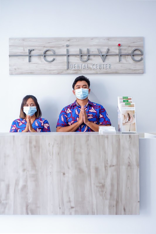 Rejuvie Dental Center reception staff in traditional Balinese batik uniforms giving a welcoming greeting at the front desk