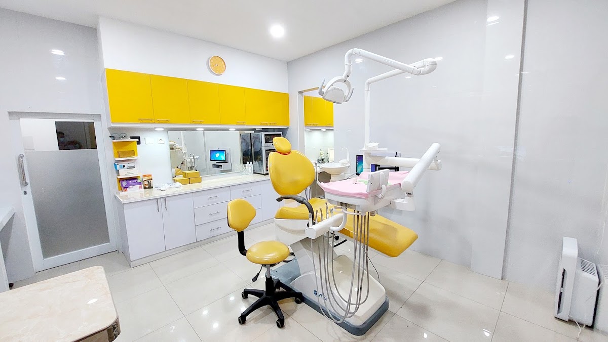A modern, well-lit dental treatment room featuring a bright yellow dental chair and matching cabinetry against clean white walls, creating a cheerful and professional atmosphere.
